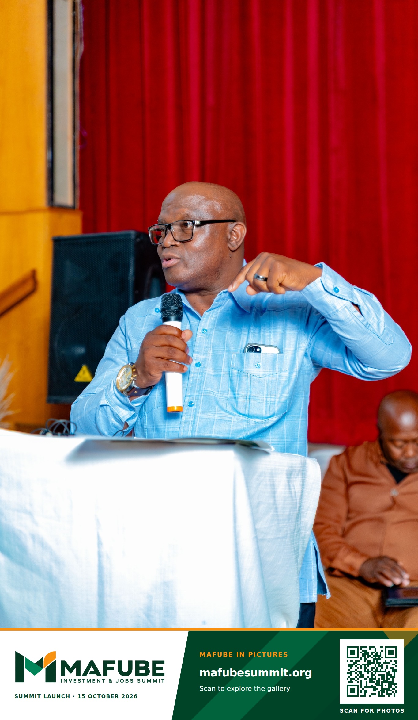 A speaker gestures while addressing the hall from the podium, with the Mafube Investment & Jobs Summit photo footer